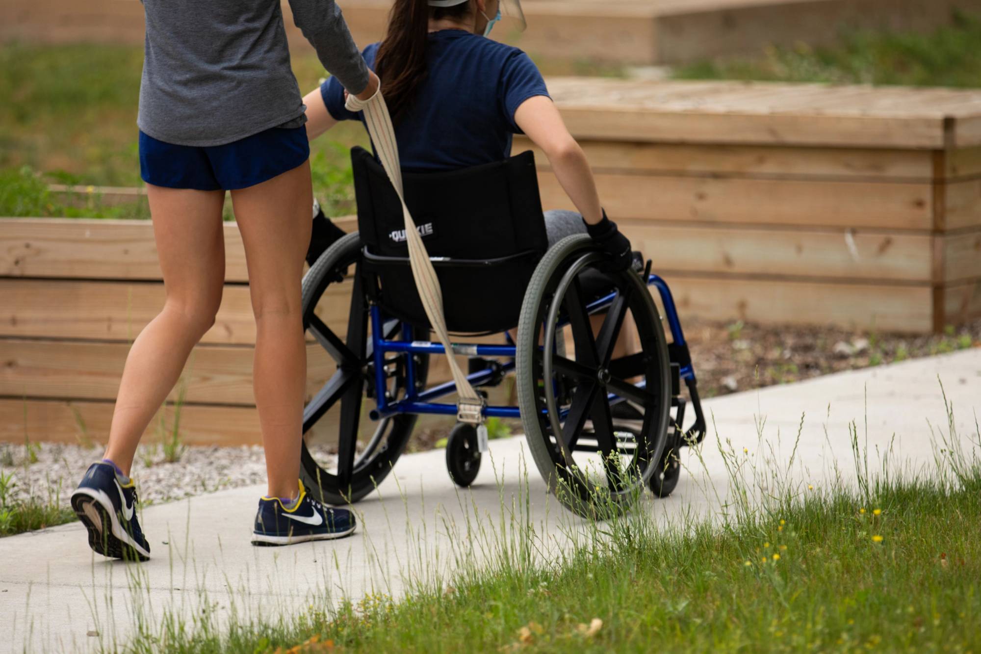 Person pushing another person in wheelchair on sidewalk